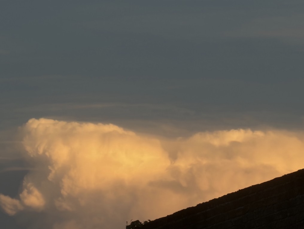 Sunset-lit clouds glowing orange under a grey-blue sky, a rooftop edge in silhouette