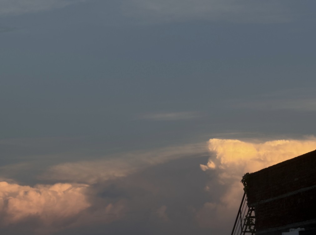 Orange clouds rising behind the dark corner of a brick building with a ladder, seen from the balcony
